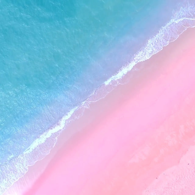 aerial view of blue waves crashing on pink sand beach