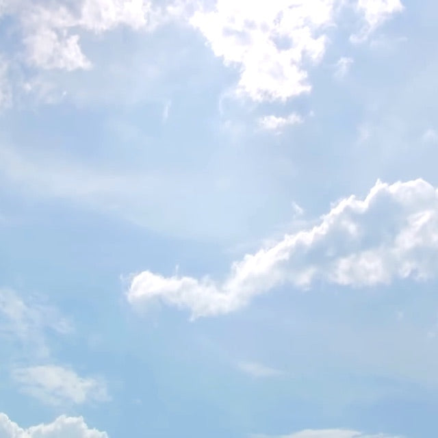 white puffy clouds in light blue sky with bright sunshine